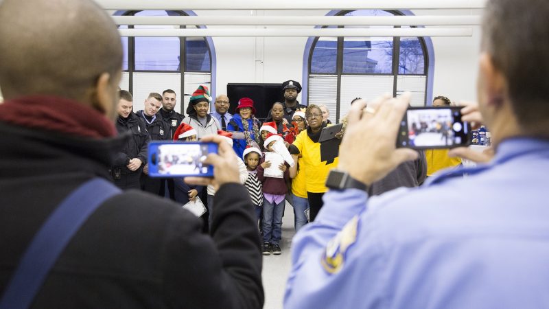 Marcell Basett (left), public relations for the Police Advisory Commission, and Officer Joe Lukaitis, co-founder of the Caroling with a Cop event, take group photographs of the community members and police officers who showed up to sing Christmas carols together on December 7. (Rachel Wisniewski for WHYY)