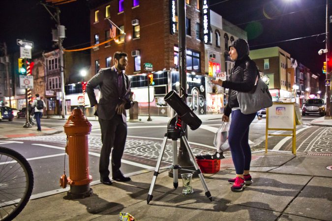 Bill Green (left) dispenses moon facts to revelers at 4th and South Streets. (Kimberly Paynter/WHYY)