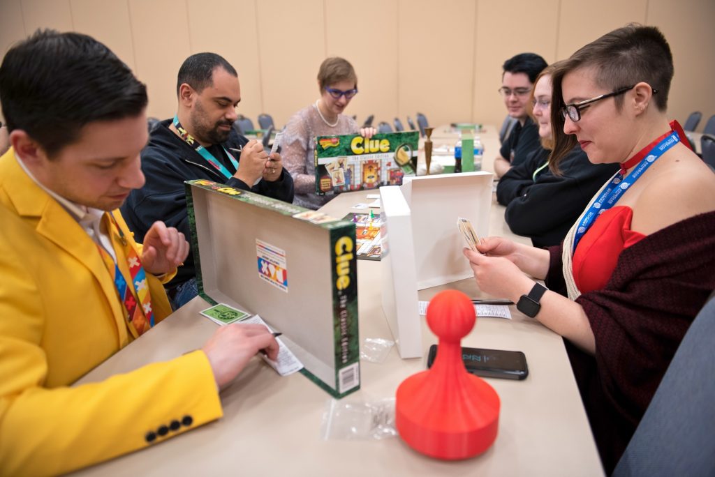 A group of convention goers, some dressed as Colonel Mustard, Miss Scarlett and Mrs. Peacock, participate in a Clue tournament at PAX Unplugged.)
