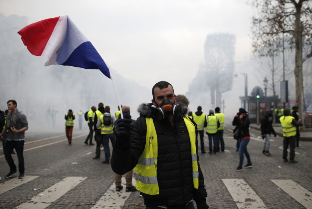 France Protests A demonstrator waves a French flag on the Champs-Elysees avenue Saturday, Dec. 8, 2018 in Paris. Crowds of yellow-vested protesters angry at President Emmanuel Macron and France's high taxes tried to converge on the presidential palace Saturday, some scuffling with police firing tear gas, amid exceptional security measures aimed at preventing a repeat of last week's rioting. (Rafael Yaghobzadeh/AP)