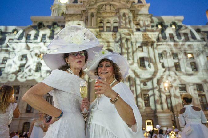 Zarbeth Teelucksingh (right) and a friend show off their hats at Le Dîner en Blanc on Aug. 16, 2018. (Jonathan Wilson for WHYY)
