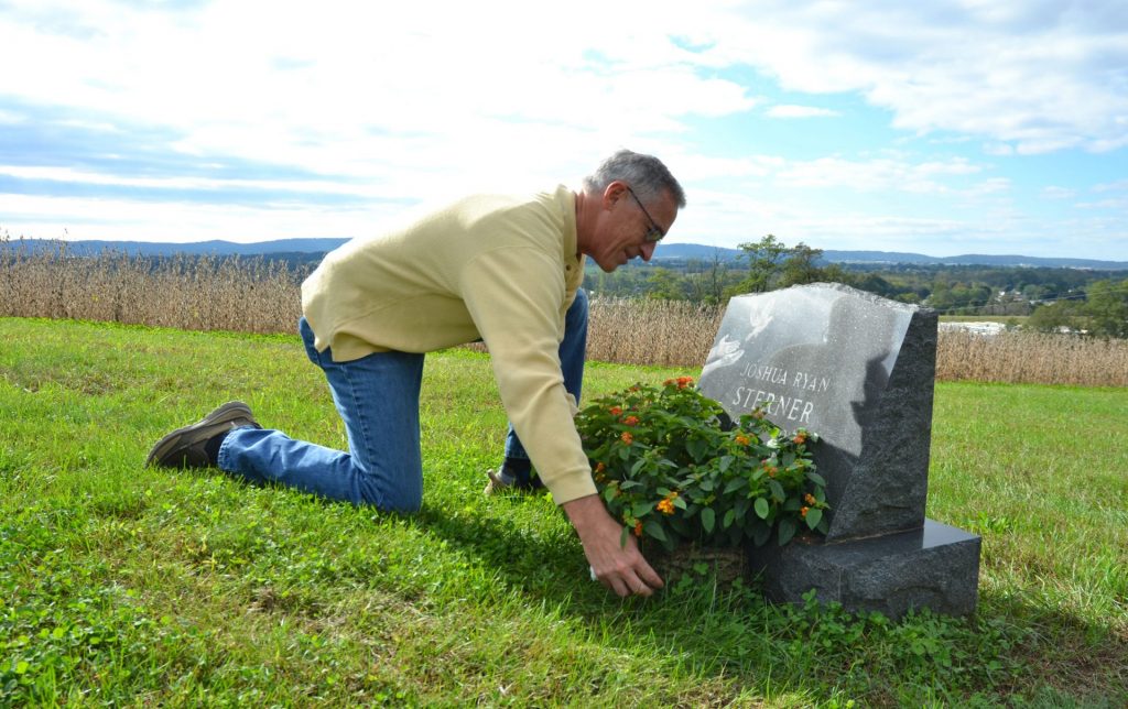 Jeff-Sterner-use-cropped-1920×1207 Jeff Sterner adjusts a flower display on his son Joshua’s grave. Josh was 19 in 2012 when he died by suicide. (Brett Sholtis / Transforming Health)