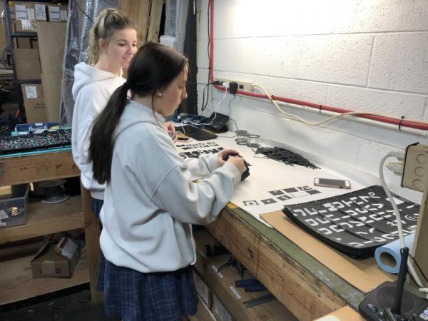 Megan Smith and Mackenzie Waters, assembly technicians at Oat Foundry and sophomores at Nazareth Academy in Philadelphia, snap out printed characters that will be used to build a split-flap display. (Meir Rinde for PlanPhilly)