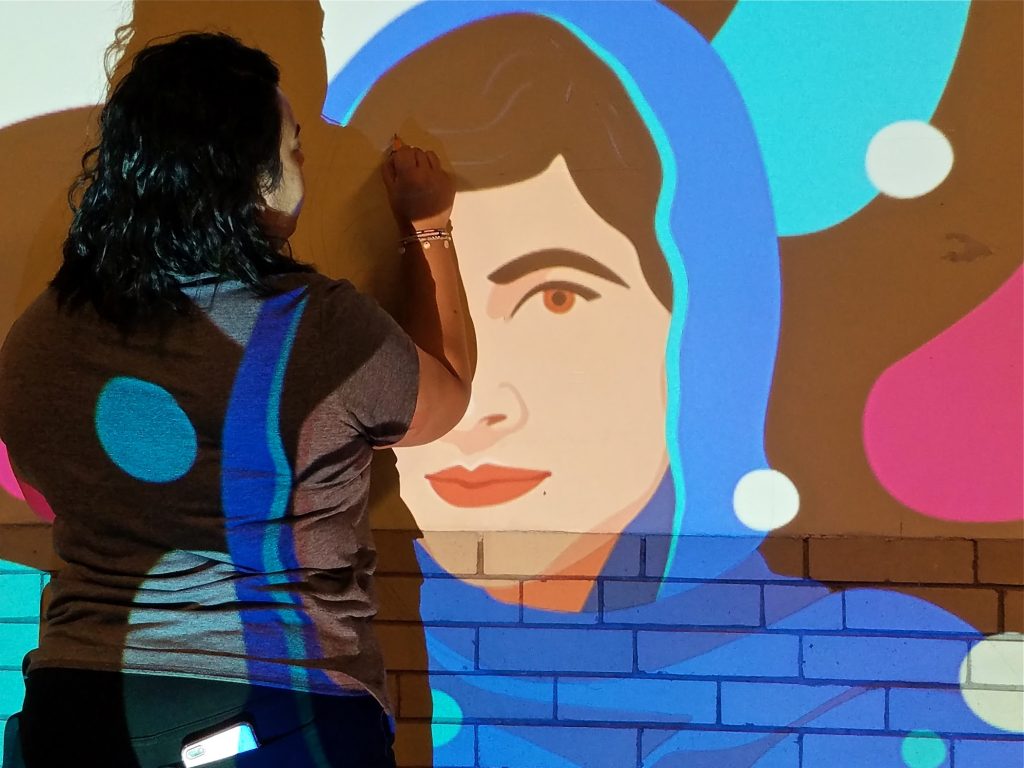 2019 01 16-p crimmins-anisa shafiq-kensington high school-100 murals mlk day of service Anisa Shafiq uses a slide projector to mark out a mural of Malala Yousafzai in a hallway of Kensington High School.