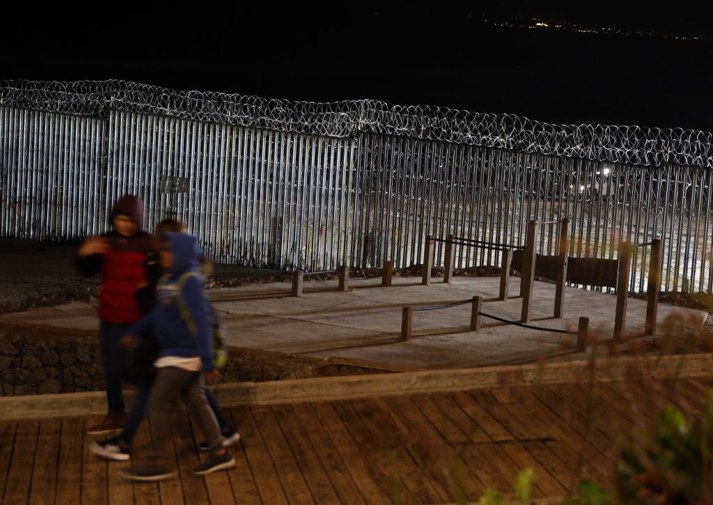Central American Migrant Caravan Floodlights from the U.S, illuminate the border wall, topped with razor wire, as a people pass Monday, Jan. 7, 2019, at the beach in Tijuana, Mexico. With no breakthrough in sight, President Donald Trump will argue his case to the nation Tuesday night that a