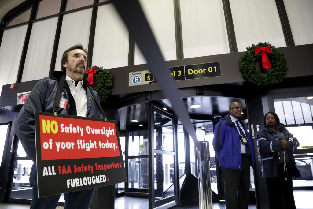 APTOPIX Government Shutdown Federal Aviation Administration employee Michael Jessie, who is currently working without pay as an aviation safety inspector for New York international field office overseeing foreign air carriers, holds a sign while attending a news conference at Newark Liberty International Airport, Tuesday, Jan. 8, 2019, in Newark, N.J. U.S. Sens. Cory Booker and Bob Menendez called a news conference at the airport to address the partial government shutdown, which is keeping some airport employees working without pay. (Julio Cortez/AP)