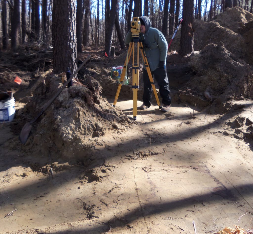 100_2689 John Potts is using a total station to map the site. Graves can be seen as grey-ish stains in the soil. (Jill Showell/Edward Otter, Inc.)