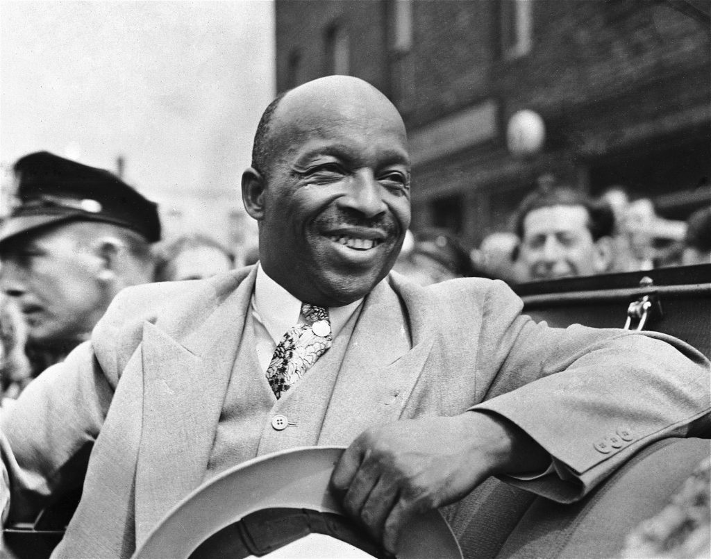 American-African spiritual leader Father Divine smiles as he leads a parade of his followers from Harlem to the docks in New York, on Aug. 20, 1936, to board the paddle-steamer City of Kennsburg to take them on the first stage of their great trek to their new camp in Ulster County, New York State. (AP Photo)