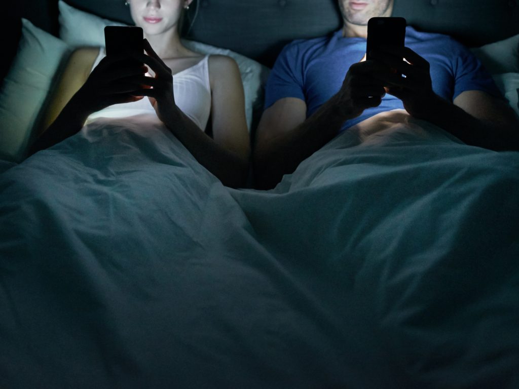 A couple side by side in bed, each looking at their cell phones. (AJ_Watt/Getty Images)