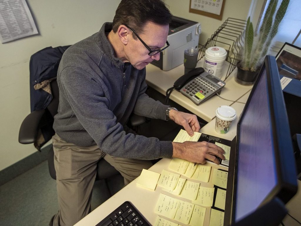 Army veteran Chris Riga survived multiple blast injuries in deployments in Afghanistan and Iraq. He rearranges sticky notes on his desk to assist him in remembering tasks he has to do throughout the day at his job as patient experience coordinator at the Northampton VA Medical Center in Leeds, Mass. (Jesse Costa/WBUR)