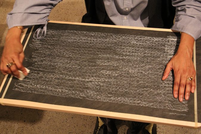 Sonya Clark makes a chalk rubbing of the Confederate truce flag, an activity available to visitors to her exhibit at the Fabric Workshop and Museum. (Emma Lee/WHYY)