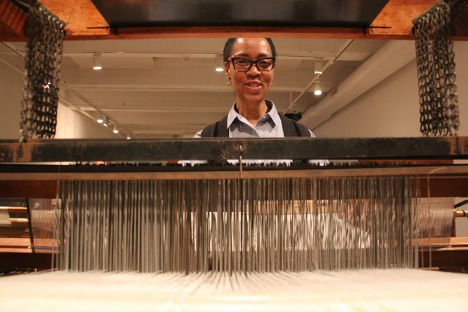 Sonya Clark sits at one of nine looms set up to weave a tea towel resembling the Confederate truce flag. Visitors will be able to add to the work. (Emma Lee/WHYY)