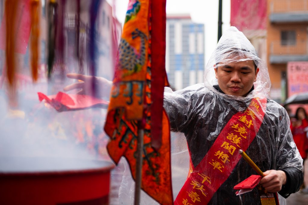 20190331_WHYY_Hoyu Festival_104 Zhang Wen tosses lit firecrackers into a barrel as part of the Hoyu Folk Culture Festival parade in Philadelphia's Chinatown on Sunday, March 31, 2019. (Kriston Jae Bethel for WHYY)