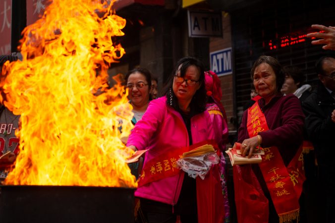 Festival-goers toss paper money into flames as a way to honor their ancestors during the Hoyu Folk Culture Festival in Chinatown on Sunday, March 31, 2019. (Kriston Jae Bethel for WHYY)