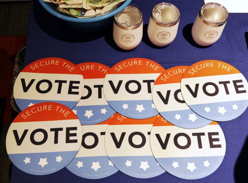 AP_18202054940250-1920×1417 Computer mouse pads with Secure the Vote logo on them are seen on a vendor's table at a convention of state secretaries of state Saturday, July 14, 2018, in Philadelphia. (Mel Evans/AP Photo)