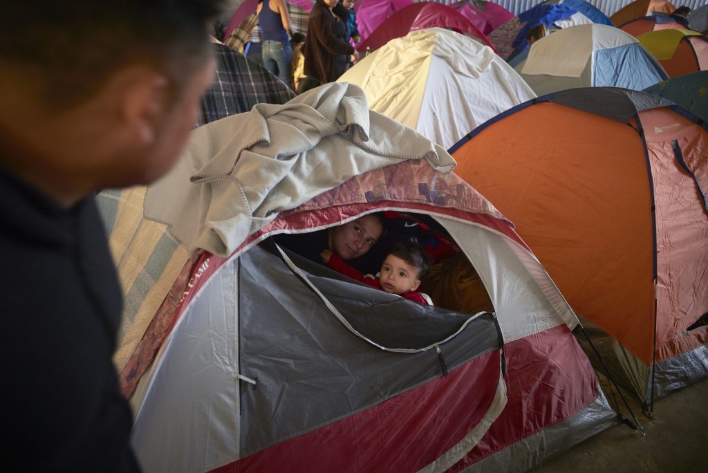 APTOPIX US Mexico Asylum In this March 5, 2019, image, Ruth Aracely Monroy, (center), looks out of the family's tent alongside her 10-month-old son, Joshua, as her husband, Juan Carlos Perla, (left), passes inside a shelter for migrants in Tijuana, Mexico. (Gregory Bull/AP Photo)