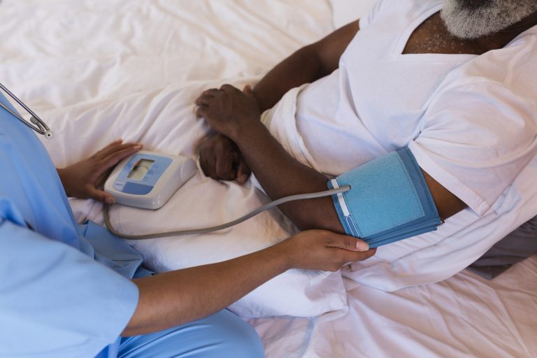 Close-up of African American female doctor measuring blood pressure of senior African American man at home