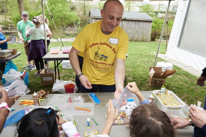 Nick Timer, a volunteer at Autism Awareness day at the Philadelphia Zoo, hands out art materials to children at an arts and crafts table at the event. (Natalie Piserchio for WHYY)