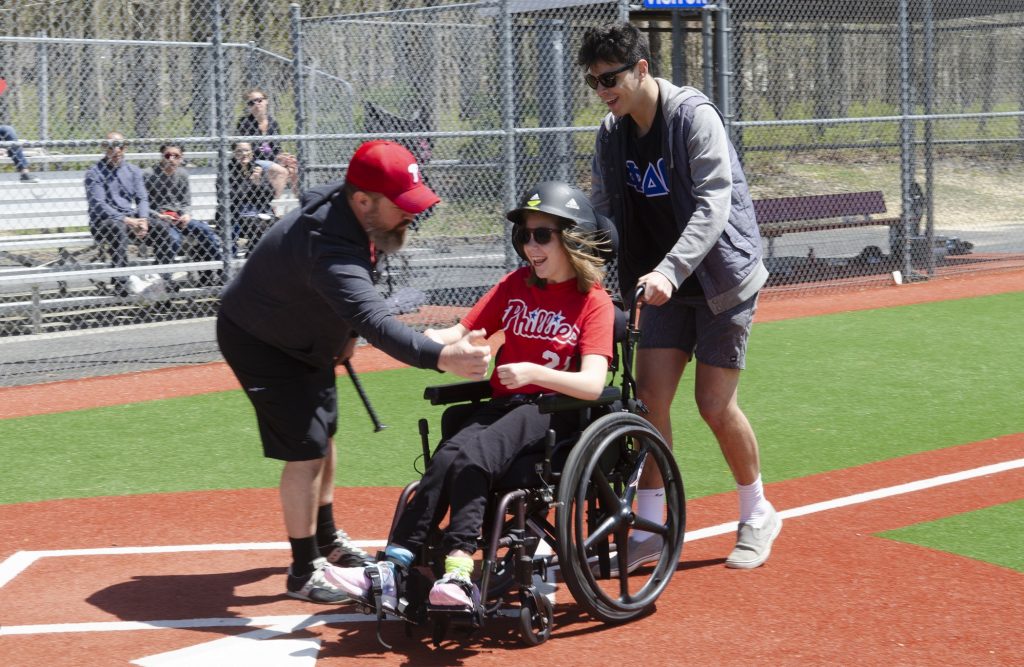 2019 04 27-a smedile-rob reed devon reed baily otto-absecon-field of dreams baseball Rob Reed congratulates Devon Reed as she crosses home plate with help from Baily Otto, a volunteer from Stockton University, during opening day at The South Jersey Field of Dreams in Absecon, New Jersey. The Field of Dreams is a place where physically and mentally disabled children and adults can participate in the game of baseball. (Anthony Smedile for WHYY)