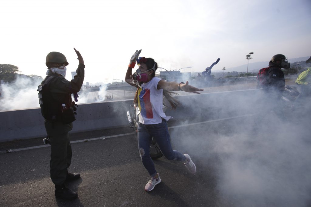 APTOPIX Venezuela Political Crisis An opponent to Venezuela's President Nicolas Maduro high fives a rebel soldier on a highway overpass outside La Carlota air base amid tear gas fired by loyalist soldiers inside the base in Caracas, Venezuela, Tuesday, April 30, 2019. Venezuelan opposition leader Juan Guaidó took to the streets in Caracas with activist Leopoldo Lopez and a small contingent of heavily armed troops early Tuesday in a bold and risky call for the military to rise up and oust socialist leader Nicolas Maduro. (Boris Vergara/AP Photo)