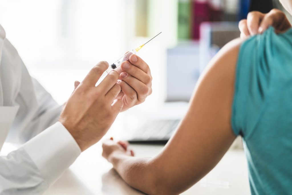 Doctor, Patient And Injection Needle. Physician Or Nurse Giving A doctor holds a vaccine syringe close to a patients exposed arm.
