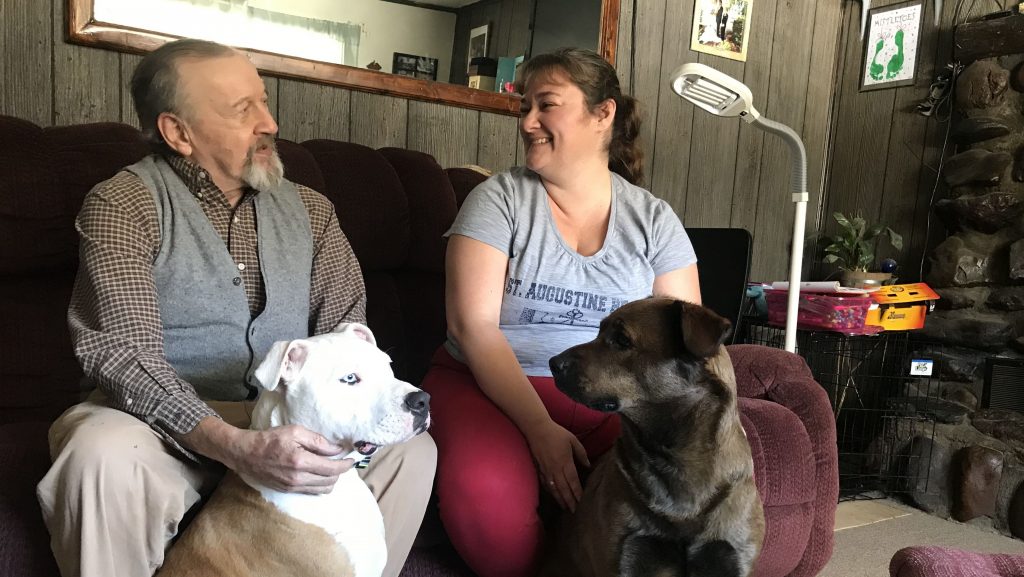 David Calderwood and Crystal Abel of Newport, Vt., sit with Abel’s dogs Mike (left) and Zoe. David lives in Crystal’s house, and she helps him with his medications and medical needs. He pays room and board, and Abel is also compensated by the state with Medicaid dollars. David Calderwood and Crystal Abel of Newport, Vt., sit with Abel's dogs Mike (left) and Zoe. David lives in Crystal's house, and she helps him with his medications and medical needs. He pays room and board, and Abel is also compensated by the state with Medicaid dollars.
(Emily Corwin/Vermont Public Radio)