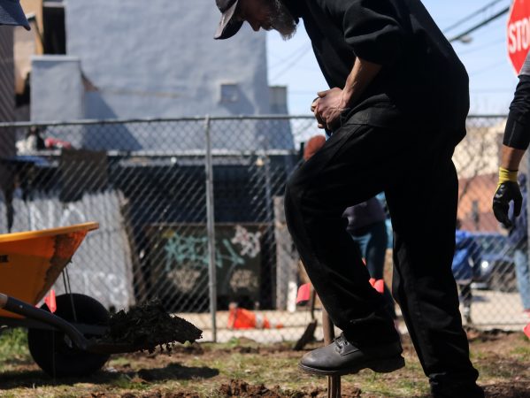 Volunteers dig shovels into the uneven ground and scoop large rocks into wheelbarrows in an effort to prepare the land for community use. (Angela Gervasi for WHYY)