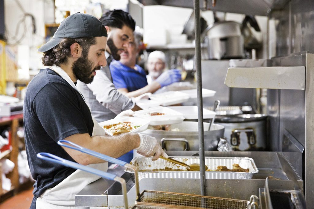 2019 05 20- r wisniewski – Anas Dabbour Abbdulah Ibrahim Munir Odeh – philadelphia Al Aqsa Al Amana – ramadan (From left) Anas Dabbour, Abbulah Ibrahim, and Munir Odeh work in an assembly line to create boxes of fish, chicken, and lamb dinners at the Al Amana Grocery on May 20, 2019. Dabbour's family established the grocery in 1993, after emigrating from Syria in 1992. (Rachel Wisniewski for WHYY)