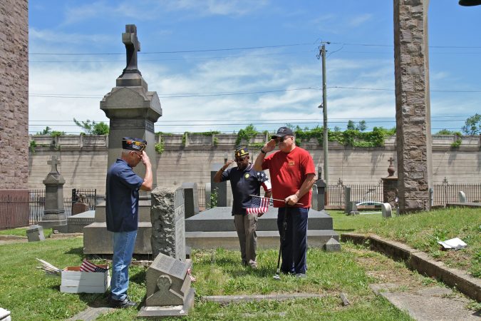 Members of American Legion Latin American Post 840 in North Philadelphia (from left) José Rivera, Darryrl Johnson and José Vargas, plant flags at the graves of veterans in St. Anne's Cemetery. (Ximena Conde/WHYY)
