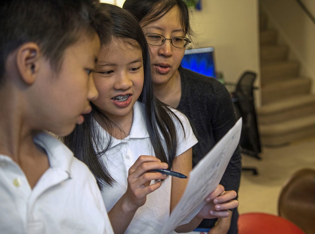 Exchange-Math Champ Vivian Loh, (center), a seventh grader at Winchester Thurston School and the first girl to win the Pennsylvania MATHCOUNTS competition, explains the solution to a math problem to her brother Vincent, 10, and their mother Debbie after they each completed a practice worksheet in the morning before school, Thursday, April 25, 2019, at their home in Squirrel Hill. (Alexandra Wimley/Pittsburgh Post-Gazette via AP)