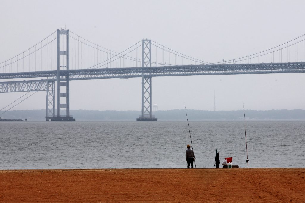 Chesapeake Bay Report Card People fish on the shore of the Chesapeake Bay, with a bridge visible in the background.