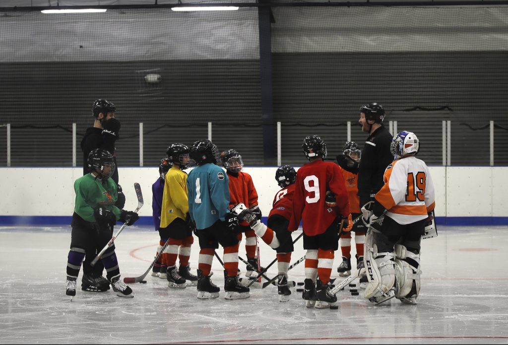 Howes Helping Hand Hockey FILE - In this Feb. 21, 2019, file photo, Malakye Johnson (1) gathers with his teammates during a Snider Hockey practice at the Scanlon Ice Rink in Philadelphia. The Philadelphia-based Snider Hockey organization named after the late Flyers owner now has over 3,000 kids in its program and almost a third are girls. Snider Hockey officials want to get to a point that boys and girls are split 50-50, and a new endeavor with the Howe Foundation is another step toward that goal. (AP Photo/Matt Rourke, File)