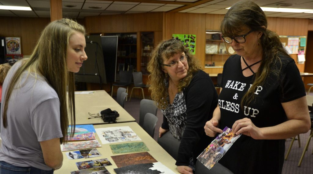 Art–e1556713501175-1920×1068 Mt. Aloysius College student Kylee Clawson, at left, and Pamela Townsend, center, look at art made by Jenny Behe, at right. Clawson, a surgical technology major, is participating in the art program as part of a college class. Townsend and Behe each have struggled with behavioral illnesses and work as peer support specialists. (Brett Sholtis/Transforming Health)