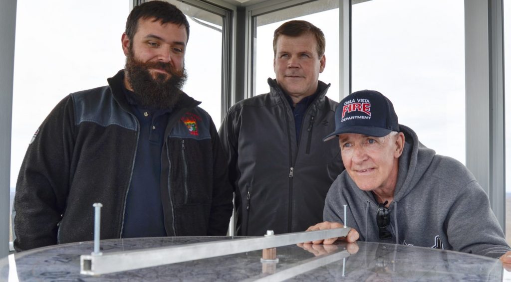 Fire-Towers-1-e1557433046642-1920×835 Officials from the Moshannon Forest District gather around the alidade, an instrument used to help personnel staffing lookout towers pinpoint the location of wildfires. From left to right, Joe Polaski, John Hecker and Larry Bickel stand in the new Chestnut Ridge tower. (Amy Sisk / StateImpact Pennsylvania)