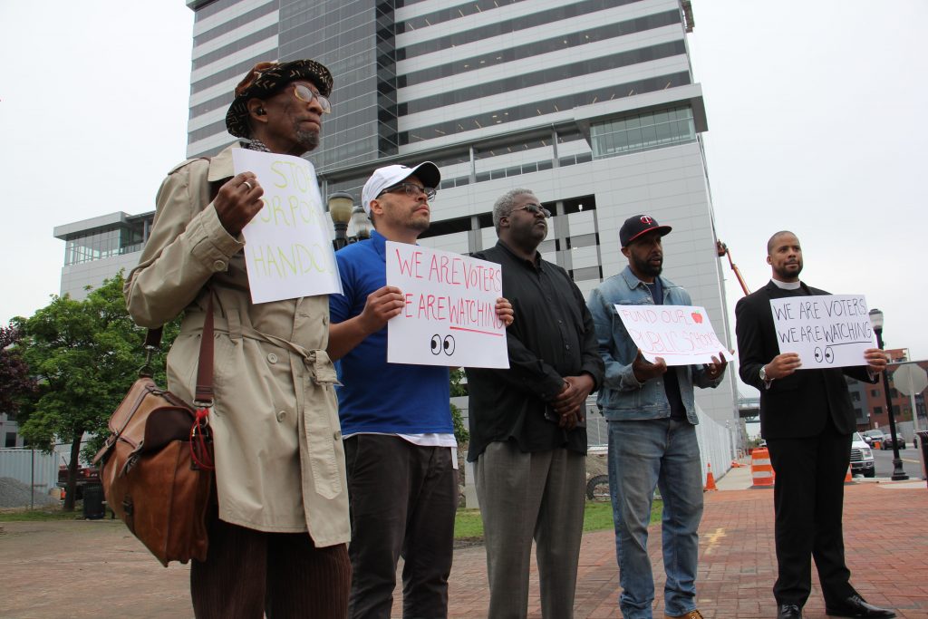 Image uploaded from iOS A small group of protesters gather outside Camden’s newest corporate high rise, demanding that beneficiaries of state tax breaks demonstrate what they’re doing to help Camden residents. (Emma Lee/WHYY)