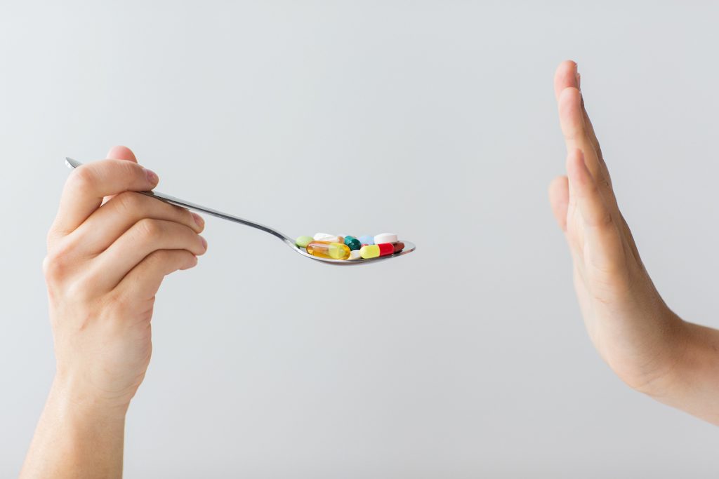 medicine, healthcare and people concept – close up of female hand holding spoon with pills Image: Bigstock/dolgachov