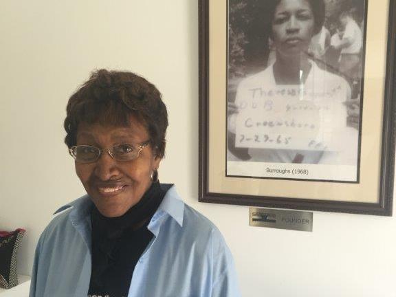 Civil rights “foot soldier” Theresa Burroughs in 2016, in front of a photo of the day she was arrested in 1965. Burroughs has died at age 89. Civil rights