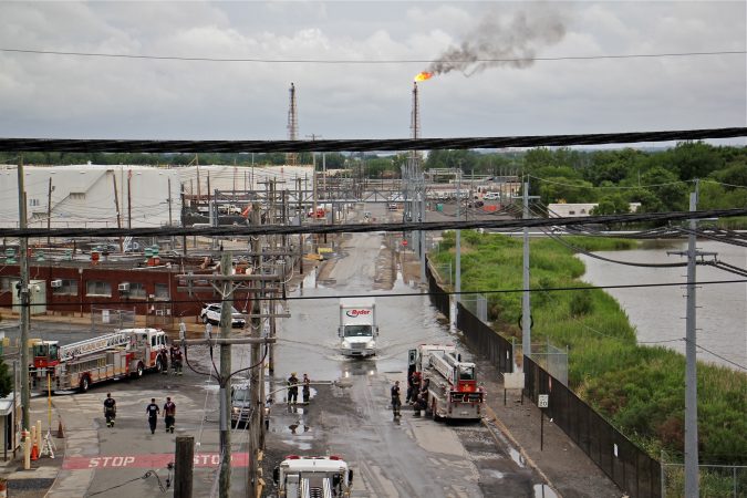 Philadelphia firefighters gather at the entrance to Philadelphia Energy Solutions Refinery, while a large flare burns off fuel to prevent it from feeding the massive fire at the refinery. (Emma Lee/WHYY)