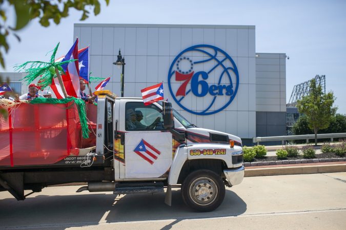 A truck with Puerto Rican flags drives past the new 76ers building as part of the San Juan Bautista Parade and Festival. The parade has been a tradition in the city for the past 62 years. (Miguel Martinez/WHYY)