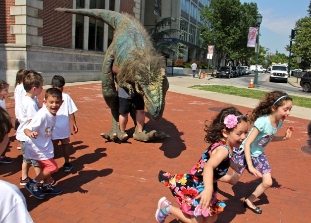 Children run shrieking from a man in a dinsaur costume