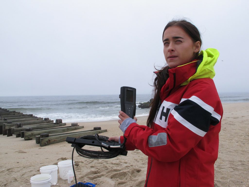 Water Testing-Surfing Beaches This May 30, 2019 photo shows Skye Post, who will be a junior at Monmouth University this fall, demonstrating water quality testing equipment near a storm drain outfall pipe on the beach in Long Branch, N.J. University researchers are studying the relationship between heavy rainfall and elevated levels of bacteria from animal waste that gets flushed into storm sewers and out in the ocean at popular surfing beaches at the Jersey shore. (Wayne Parry/AP Photo)