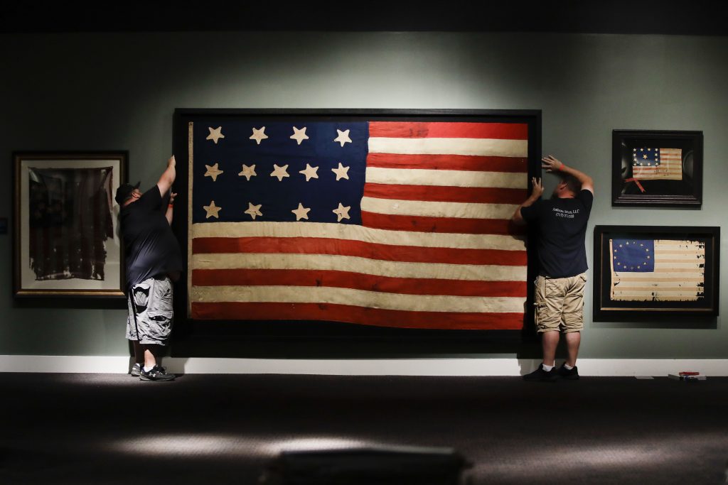 13-Star Flags In this Wednesday, June 12, 2019 photo, workmen hang a Federal Era flag as part of the new exhibit 'A New Constellation: A Collection of Historic 13-Star Flags,' at the Museum of the American Revolution in Philadelphia. (Matt Rourke/AP Photo)