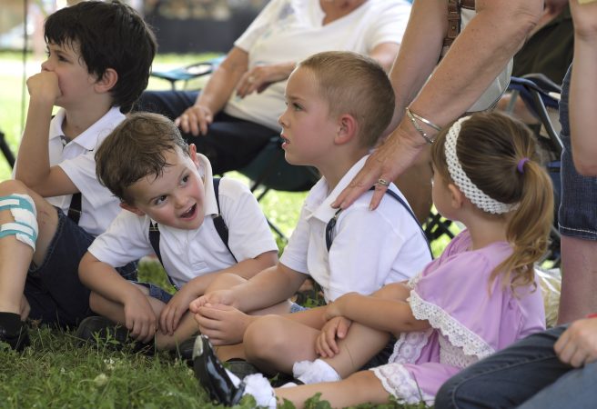 Landon Losito (left) looks over at his cousins Blaik Losito (center) and Ava Losito (right) as they sit at the side of the stage while older family members perform in the hoedown. (Matt Smith for WHYY)