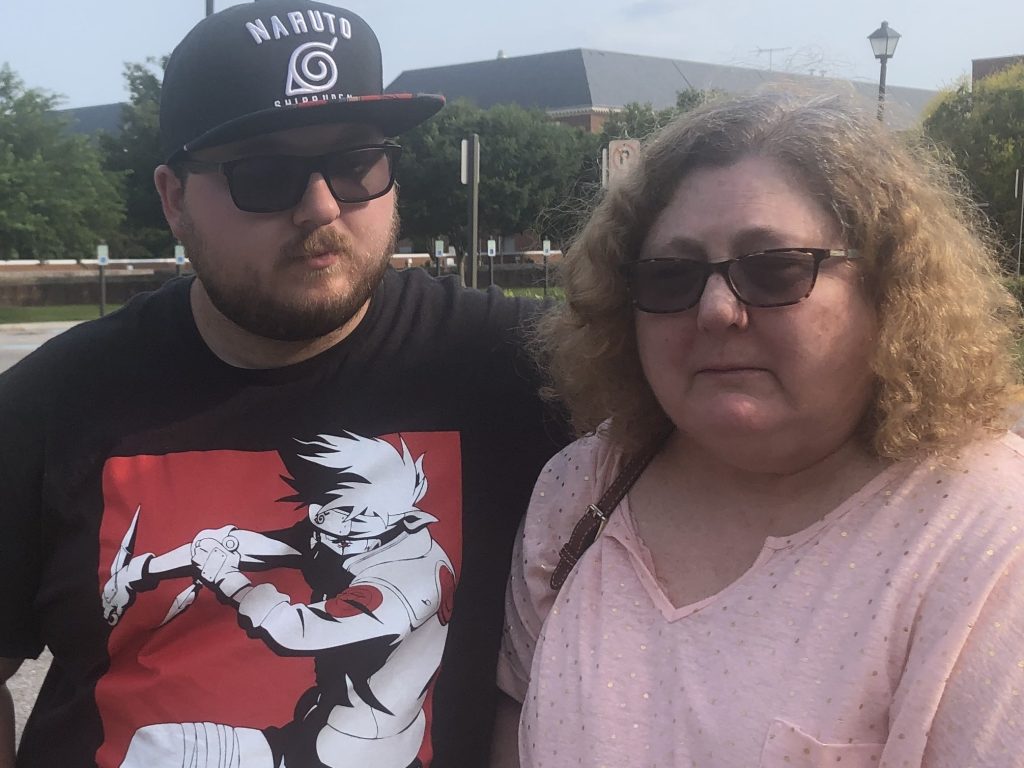 Christi Dewar, a survivor of the Virginia Beach mass shooting, stands with her son, Charles Dewar III, next to the office complex where a gunman killed 12 and injured several others on Friday. (Bobby Allyn/NPR)
