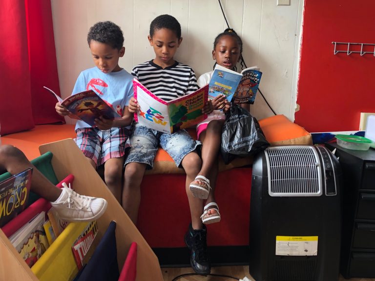 Christian Howell (center) is flanked by younger siblings Kaiden and Karima at the African Barbershop on North Market Street in Wilmington. (Cris Barrish/WHYY)