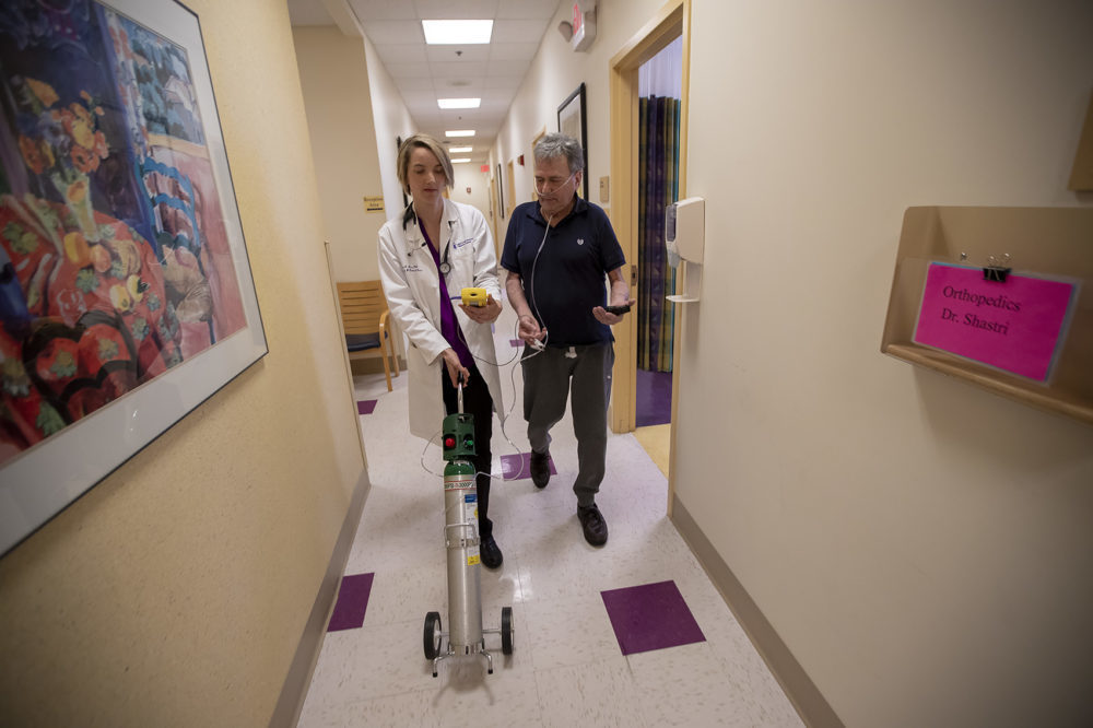 Dr. Mary Rice walks with Michael Howard at a Beth Israel Deaconess HealthCare clinic in Chealsea, Mass, as they test his oxygen levels with the addition of oxygen from a portable tank. He has COPD, a progressive lung disease that can be exacerbated by heat and humidity. Rice, who studies the health effects of air pollution, talks with Howard about his increased breathing problems and their possible link to the heat waves, increased pollen and longer allergy seasons associated with climate change. (Jesse Costa/WBUR)