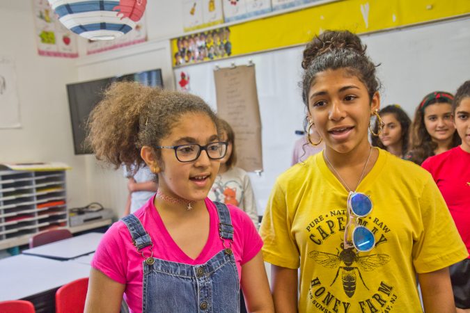 Noor Anaim (right) and Tala Takealden sing a song in Arabic at Al-Bustan camp. (Kimberly Paynter/WHYY)