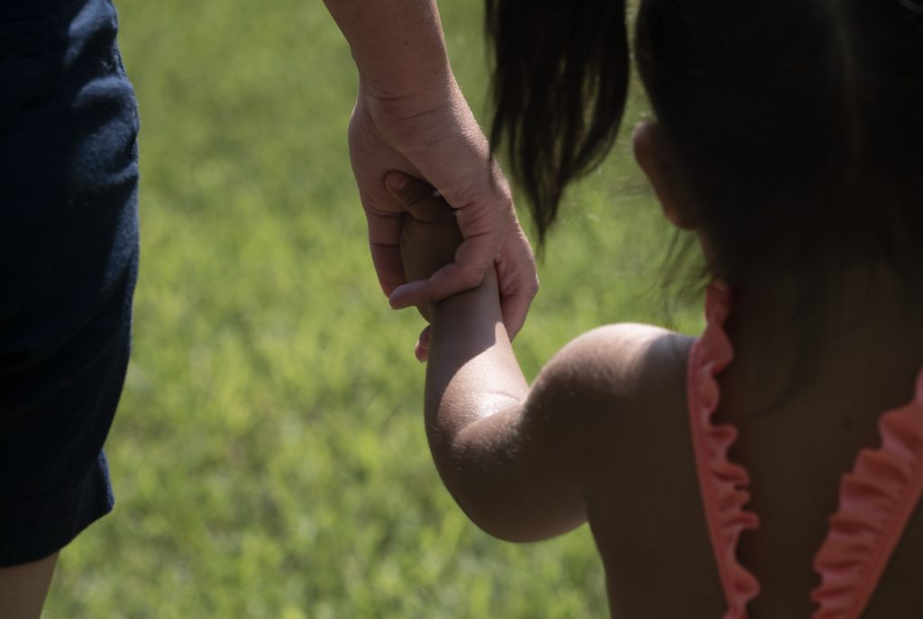 Christi holds a migrant child's hand as they walk to the swimming pool. (Shuran Huang/NPR)