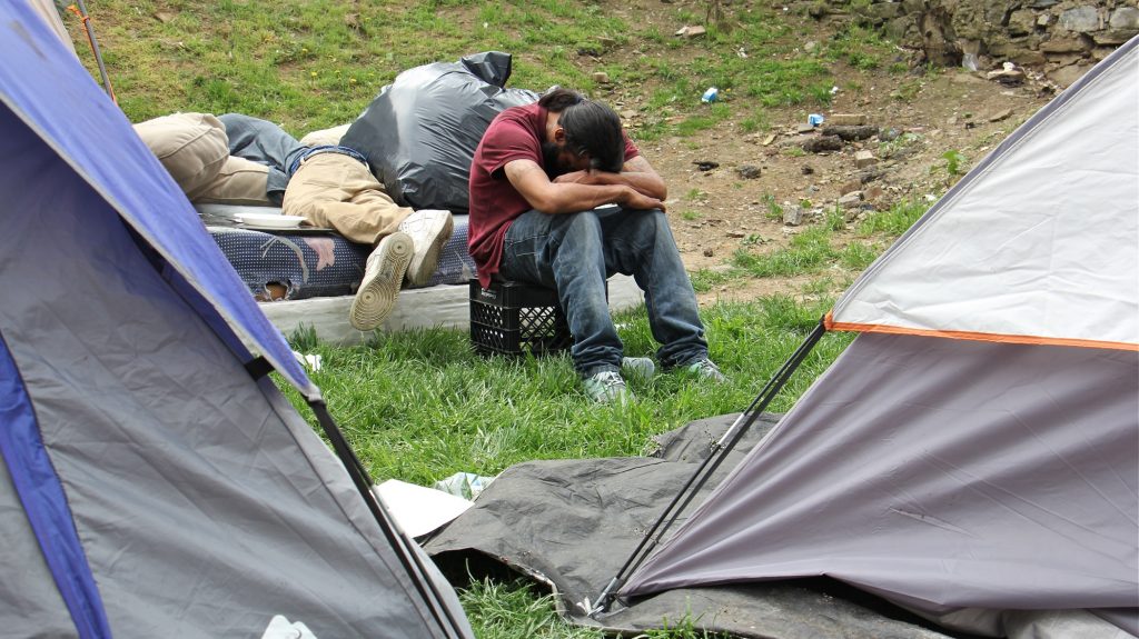 2018 05 04-e lee-philadelphia kensington avenue-heroin encampment A man rests his head on his arms in a heroin encampment in a vacant lot on Kensington Avenue on May 4, 2018. The encampment was later cleared out by the city. Pennsylvania will receive $10 million from Bloomberg Philanthropies to combat opioid addiction. The state was picked for its diverse cultural geography which could offer models for both rural and urban regions hit hard by high numbers of overdose deaths. (Emma Lee/WHYY)