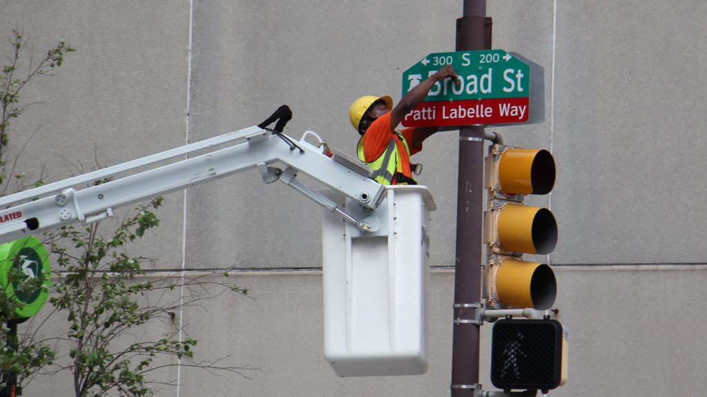 Image uploaded from iOS (7) A worker bolts on a sign changing a block of Broad Street Patti LaBelle Way. (Emma Lee/WHYY)